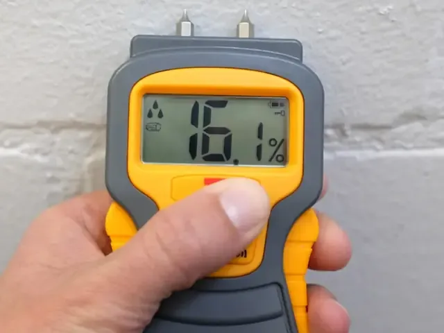 A pin moisture meter pressed into a wet wall to take a reading during an inspection