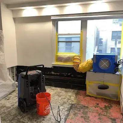 A dehumidifier and an air mover working in a room whose flooring has been pulled up