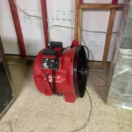 A red air mover and plastic sheeting set up in a room where the lower wall has been opened