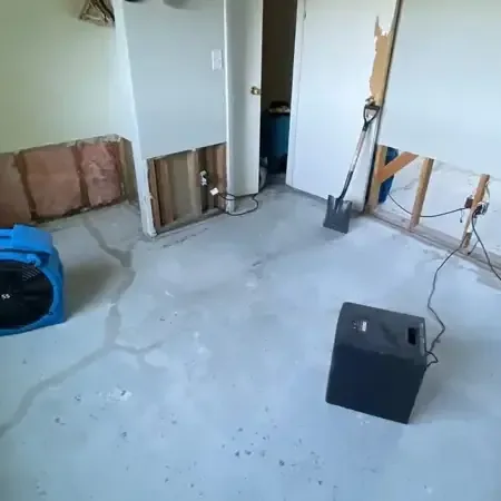 Air movers and a dehumidifier running on a bare floor in a room where the lower drywall has been cut away